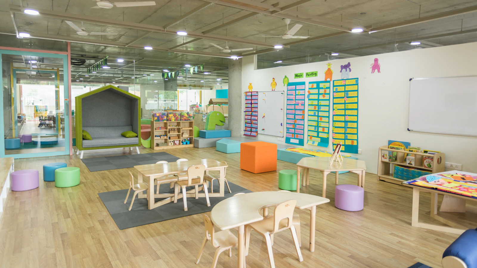 A bright, empty preschool classroom with small tables, colorful seats and wall displays