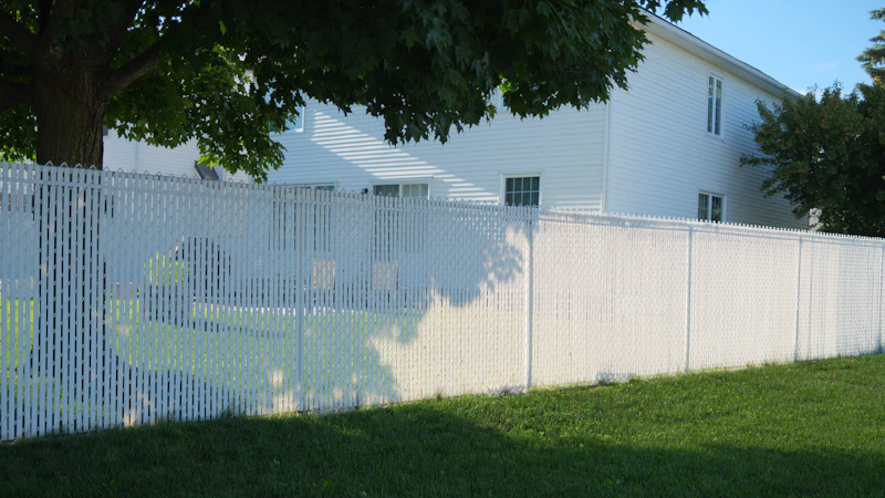 A white vinyl privacy fence along a residential lawn with a house behind it
