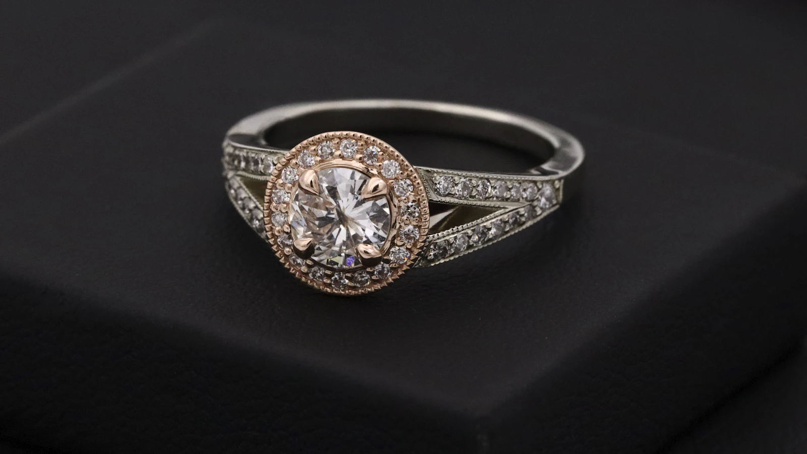 A halo diamond engagement ring displayed on a black ring box