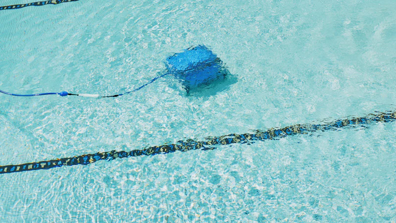 A robotic cleaner moving across the floor of a clear blue swimming pool