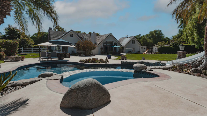 A residential pool surrounded by landscaping, palm trees and a stone deck