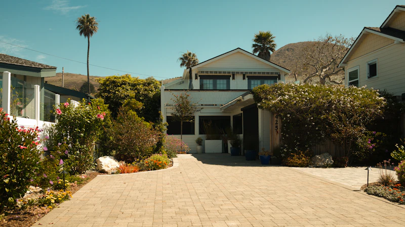 A white house with a long paver driveway, landscaping and palm trees