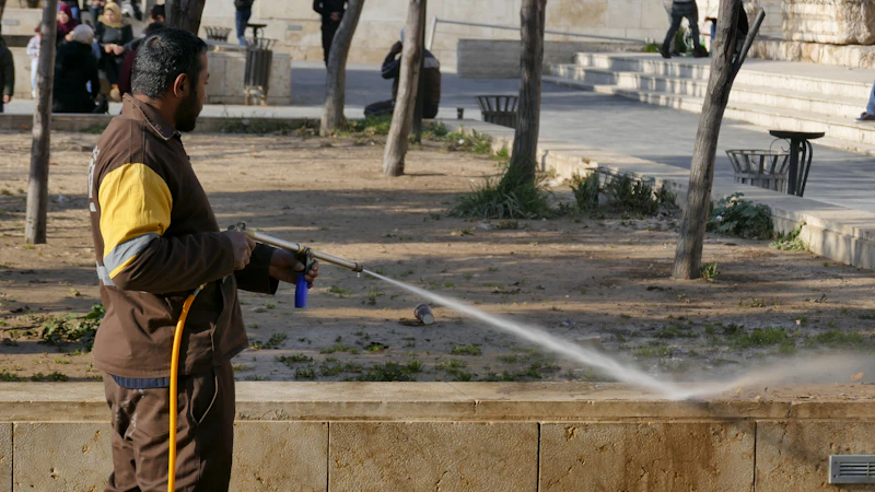 A worker spraying a high-pressure water stream across a paved plaza