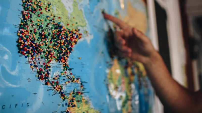 A hand pointing at a world map covered in colorful pins